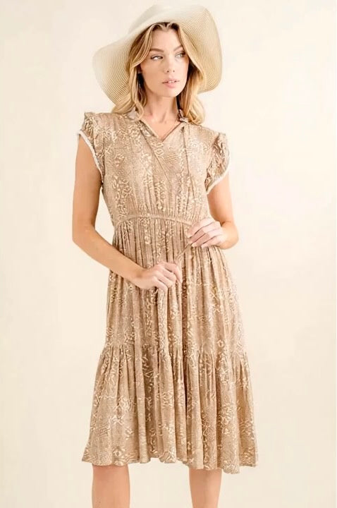 Woman wearing a gold lace dress and hat against a beige background
